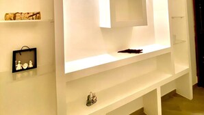 Una sala moderna con un mueble blanco grande para entretenimiento, que incluye estantes y un espacio hundido en el centro.