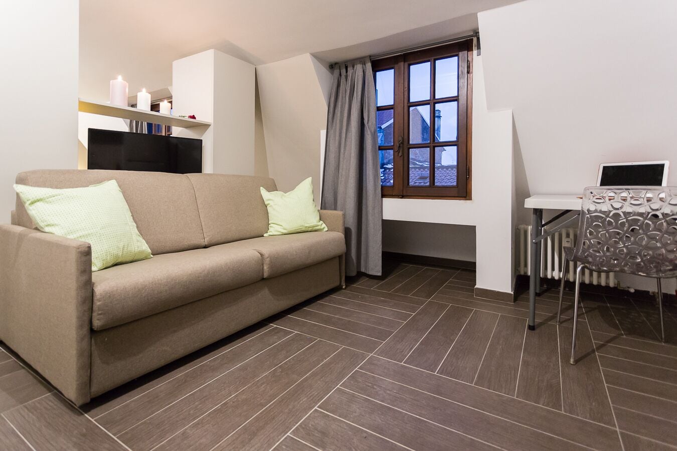 A modern living room with a sofa, a dining table with a chair, a TV, and a window with curtains.