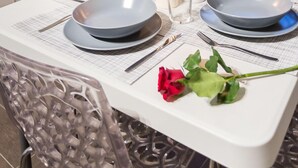 Mesa de comedor dispuesta con platos, copas y una botella de champán, con una rosa sobre la mesa.