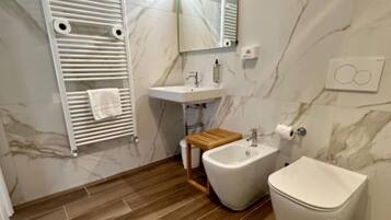 A modern bathroom with a marble wall, a wooden floor, a white sink, a bidet, and a toilet.