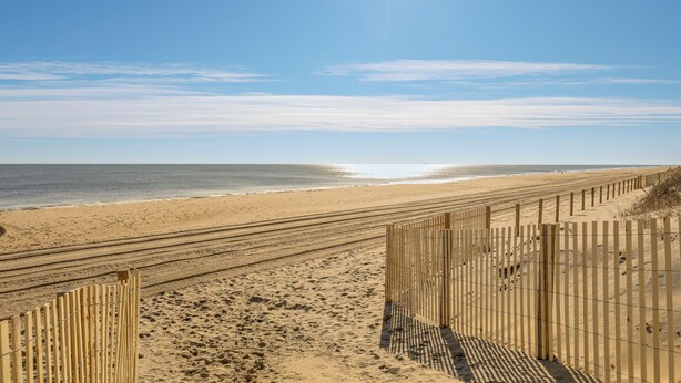 Une plage de sable avec une clôture en bois et un ciel dégagé.