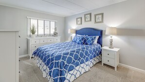 Une chambre à coucher comprenant un lit, des tables de chevet, une commode et une fenêtre avec des stores.