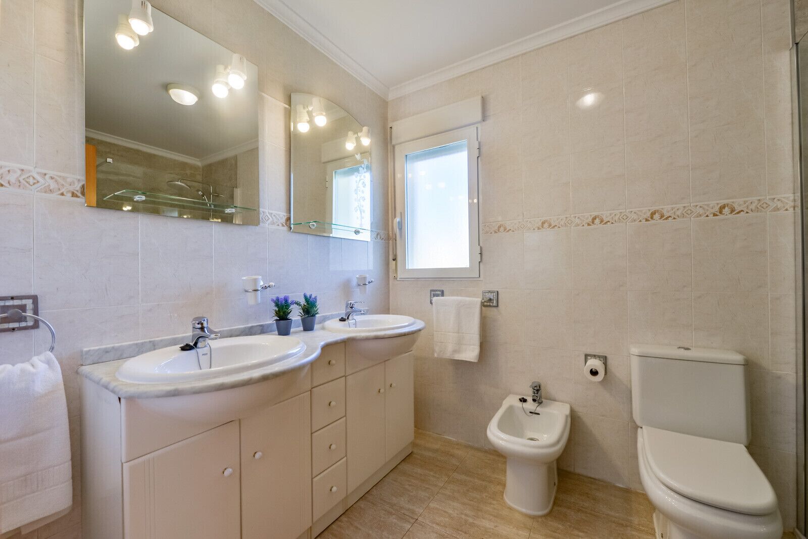 Een badkamer met twee wastafels, toilet, bidet en een grote spiegel.
