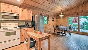Cocina de cabaña de madera con comedor, armarios de madera, un refrigerador, una estufa y un reloj en la pared.
