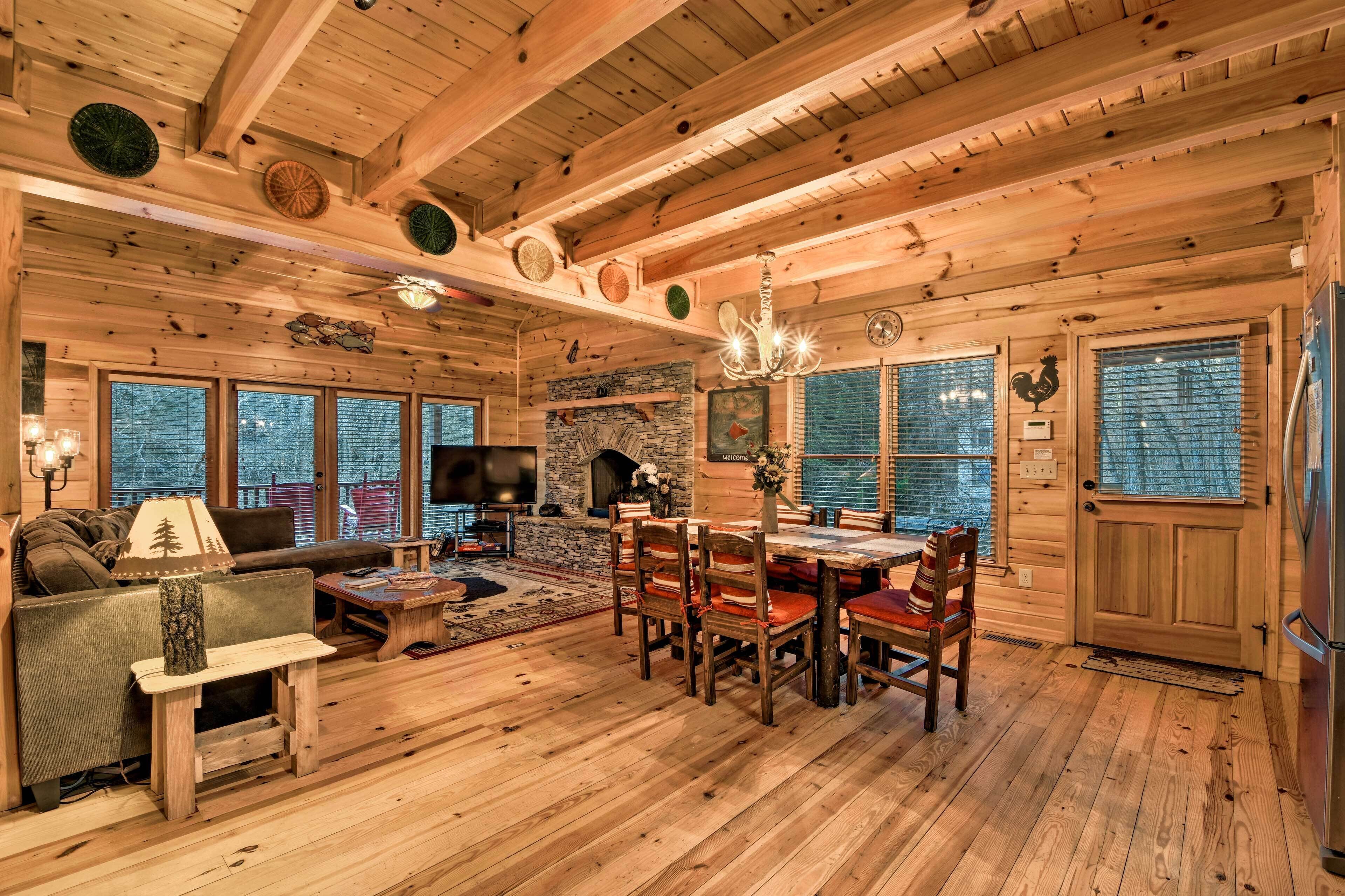 L’intérieur d’une cabane en rondins comprend un coin repas, une cheminée, un téléviseur et un mur en pierre.