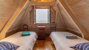 Ein gemütliches Schlafzimmer im Dachgeschoss mit zwei Betten, einem kleinen Holztisch und einem Fenster mit Blick.