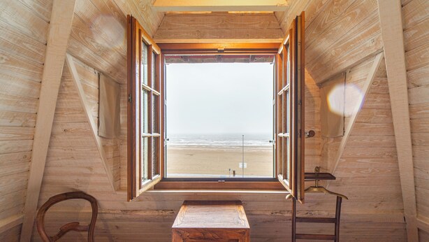 Ein Zimmer mit großem Fenster, Holzwänden, einem kleinen Holztisch, einem Stuhl und einer Leiter.