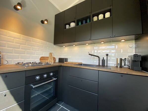 A modern kitchen with dark cabinetry, a gas stove, an oven, and a coffee machine.