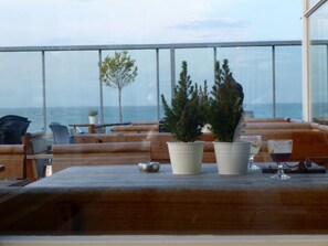 A wooden table with potted plants and glasses of drink, overlooking the sea.