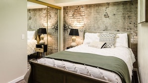 Une chambre à coucher avec un lit, deux tables de chevet, un miroir et un mur décoré d’un motif en briques.