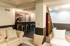 Un salon accueillant avec un mur en briques, un coin bar avec des tabourets et un escalier menant à un autre niveau.