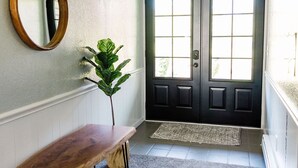 Un couloir avec un banc en bois, un miroir, une plante et une chatière bleue.