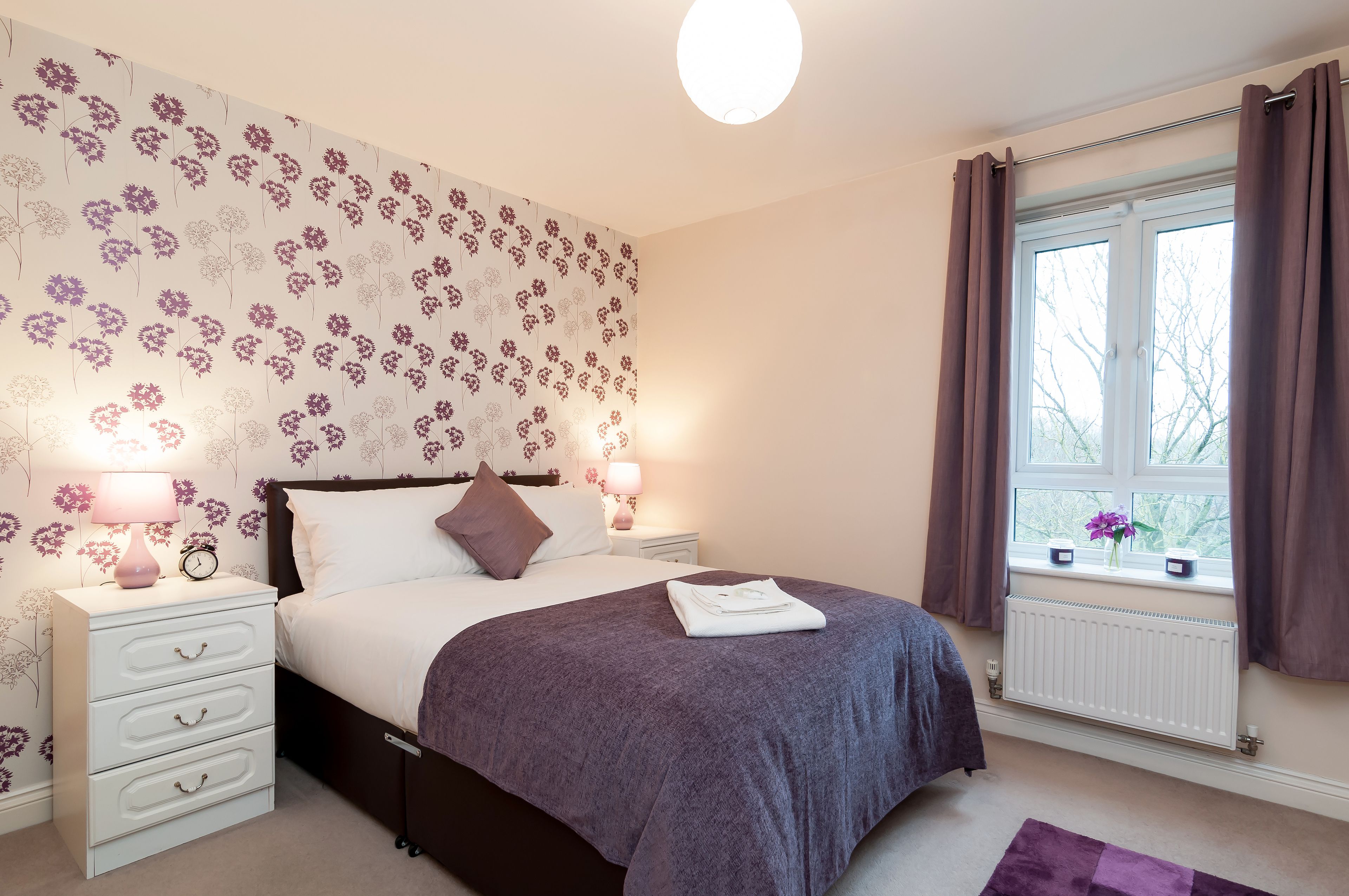 A bedroom with a bed, bedside tables, a window with curtains, and a floral wallpaper.