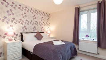A bedroom with a bed, bedside tables, a window with curtains, and a floral wallpaper.