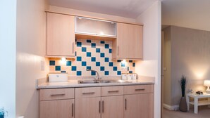 A modern kitchen with light wood cabinets, a tiled backsplash, and a countertop with a sink. - Bladon Court (Basingstoke)
