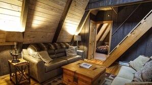 A cozy loft bedroom with a sloped ceiling, a sofa, a wooden chest, and a staircase. - Come SKI on the BEECH! Book your ski trip NOW, weekends going fast. (Beech Mountain)
