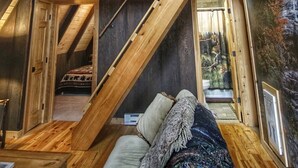 A loft-style room with a sloped ceiling, wooden beams, and a ceiling fan. There is a staircase leading to an upper level, and a large window on the right side. - Come SKI on the BEECH! Book your ski trip NOW, weekends going fast. (Beech Mountain)