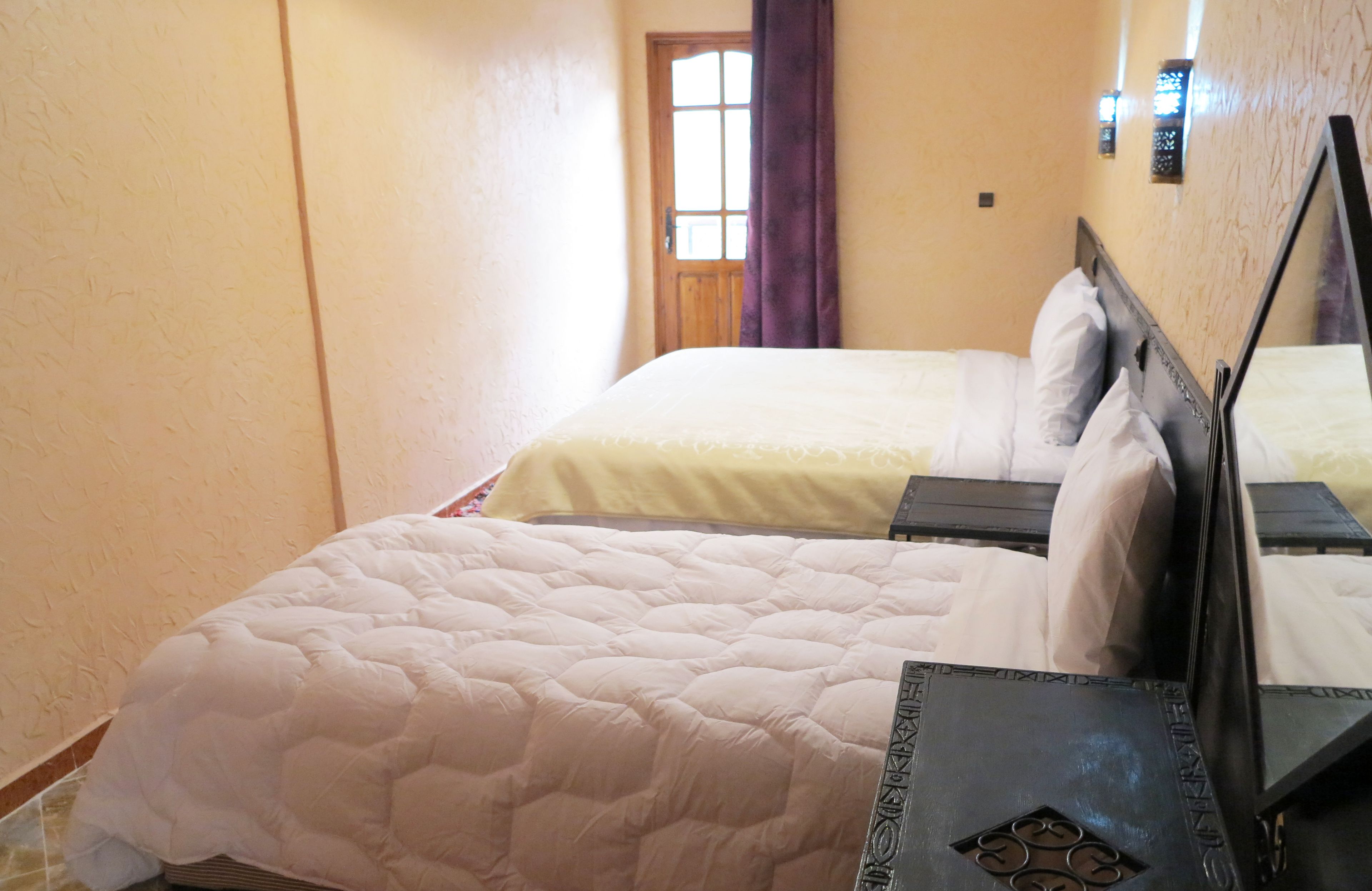 A hotel room with two beds, a wooden door, and a window with curtains.