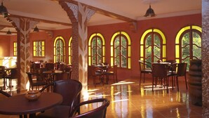 A restaurant with multiple tables and chairs, large arched windows, and a tiled floor. - Kasbah Imoula (Asni)