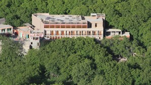 A large building with multiple floors, surrounded by dense green forest. - Kasbah Imoula (Asni)