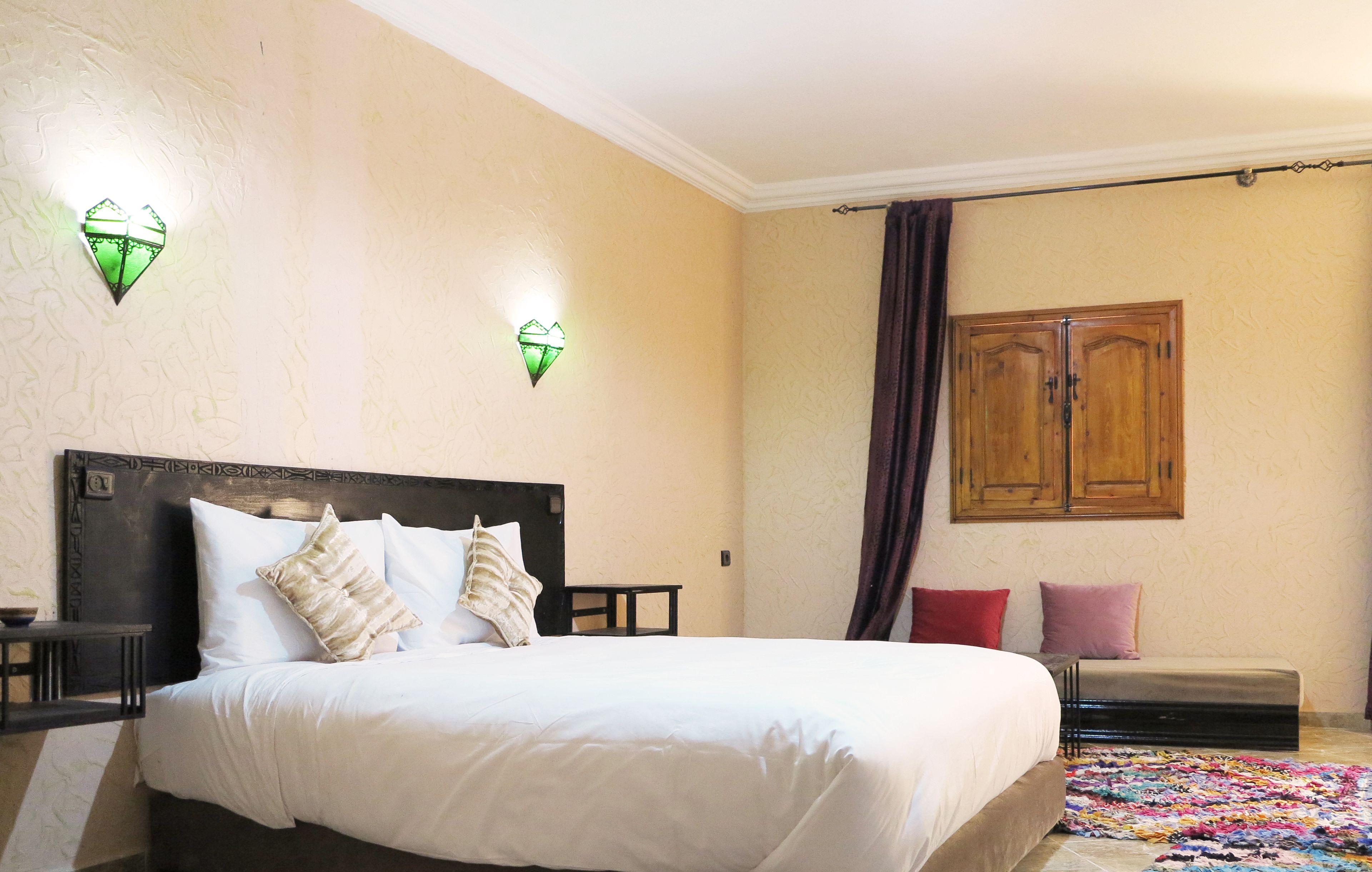 A neatly made bed with white linens, two bedside tables, a wooden wardrobe, and two wall-mounted light fixtures.