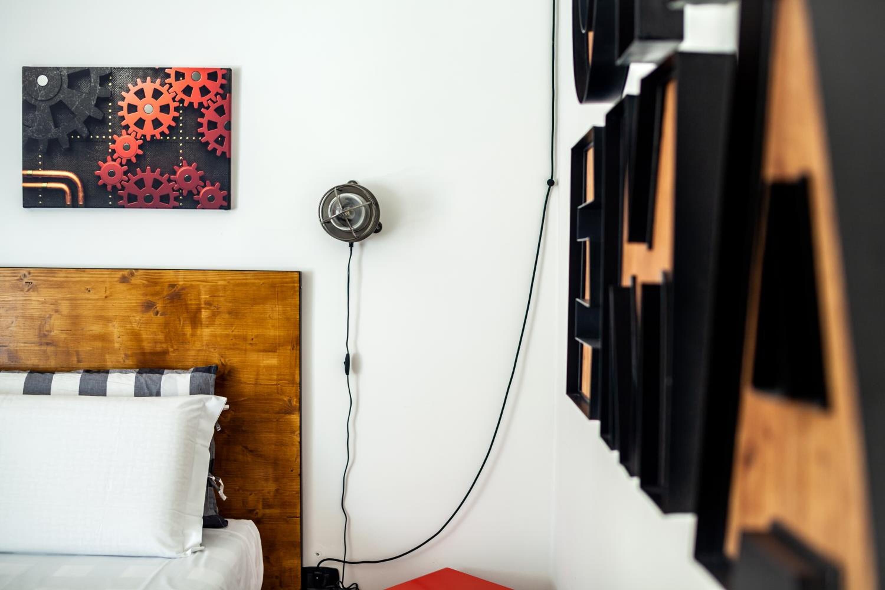 A bedroom with a wooden headboard, a bed with white and gray bedding, a wall-mounted clock, and a power outlet.