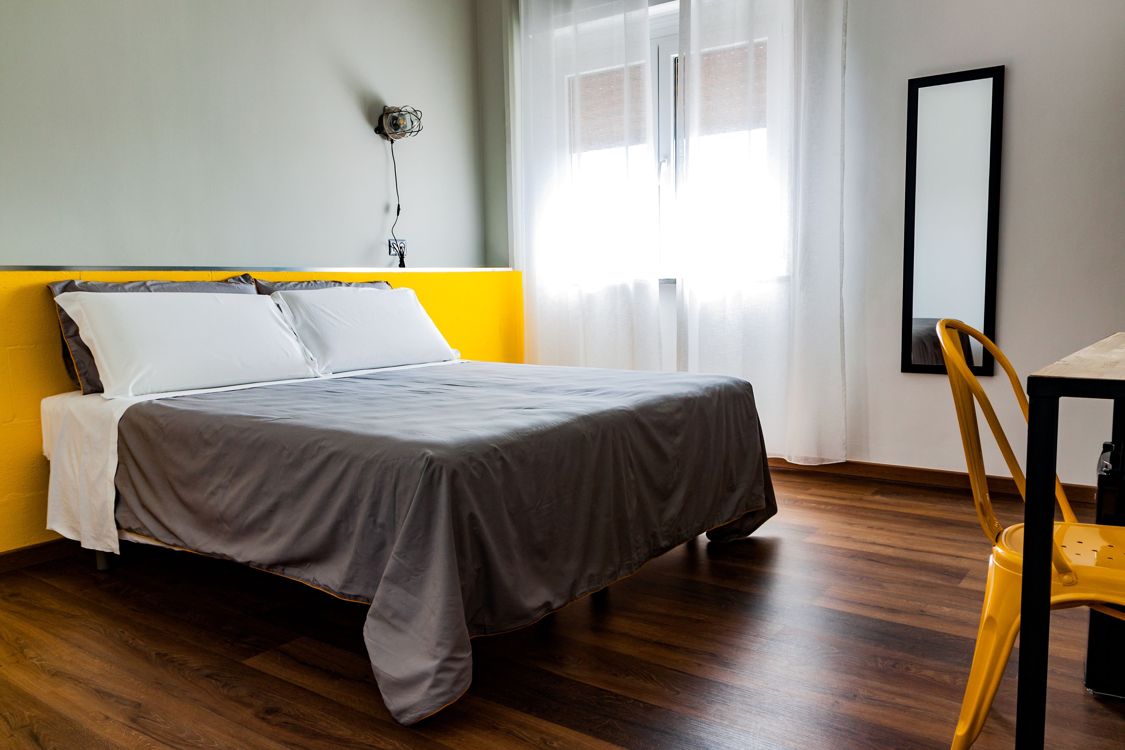A neatly made bed with a gray bedspread, a yellow headboard, and a white pillow.