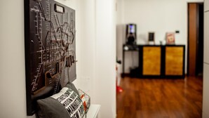 Quarto com piso de madeira, uma obra de arte na parede, um sofá com almofada e uma área de recepção ao fundo.