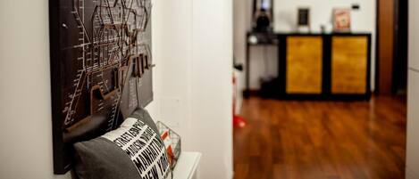 Une pièce avec un plancher en bois, une œuvre d’art accrochée au mur, un canapé avec un coussin et, au fond, un espace d’accueil.