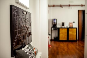 Une pièce avec un plancher en bois, une œuvre d’art accrochée au mur, un canapé avec un coussin et, au fond, un espace d’accueil.