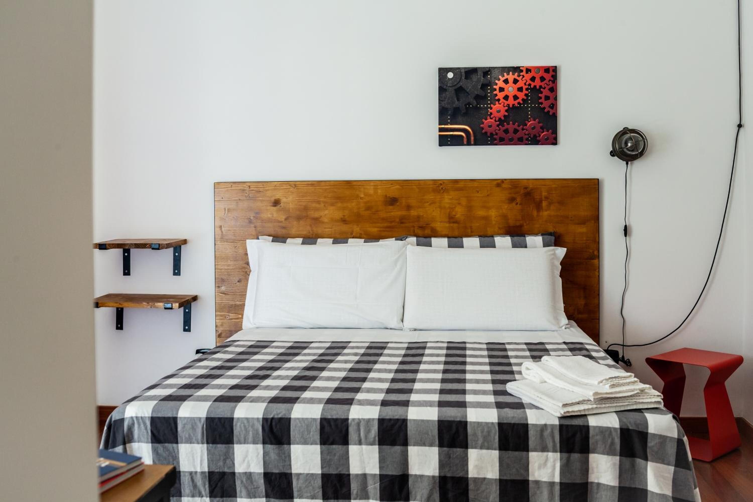 A neatly made bed with a checkered bedspread, a wooden headboard, and a wall-mounted artwork.