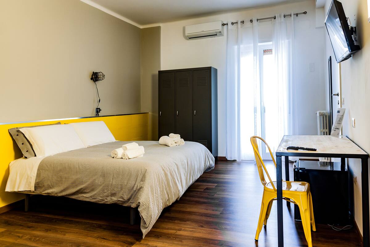 Et hotelværelse med seng, skrivebord, stol, aircondition og garderobeskab.