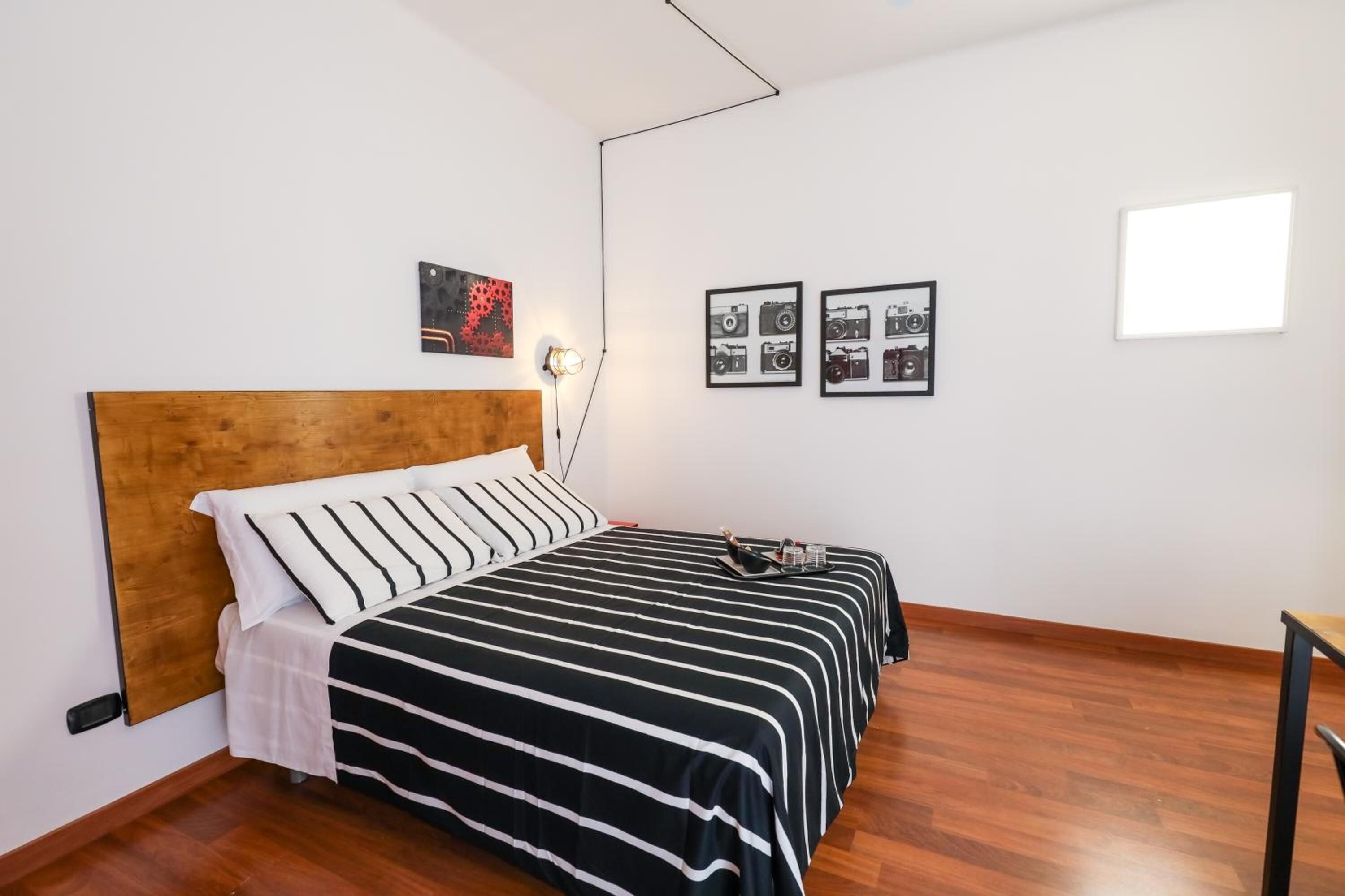 Un dormitorio ordenado con cabecera de madera, colcha a rayas blancas y negras y una mesita de noche con lámpara.