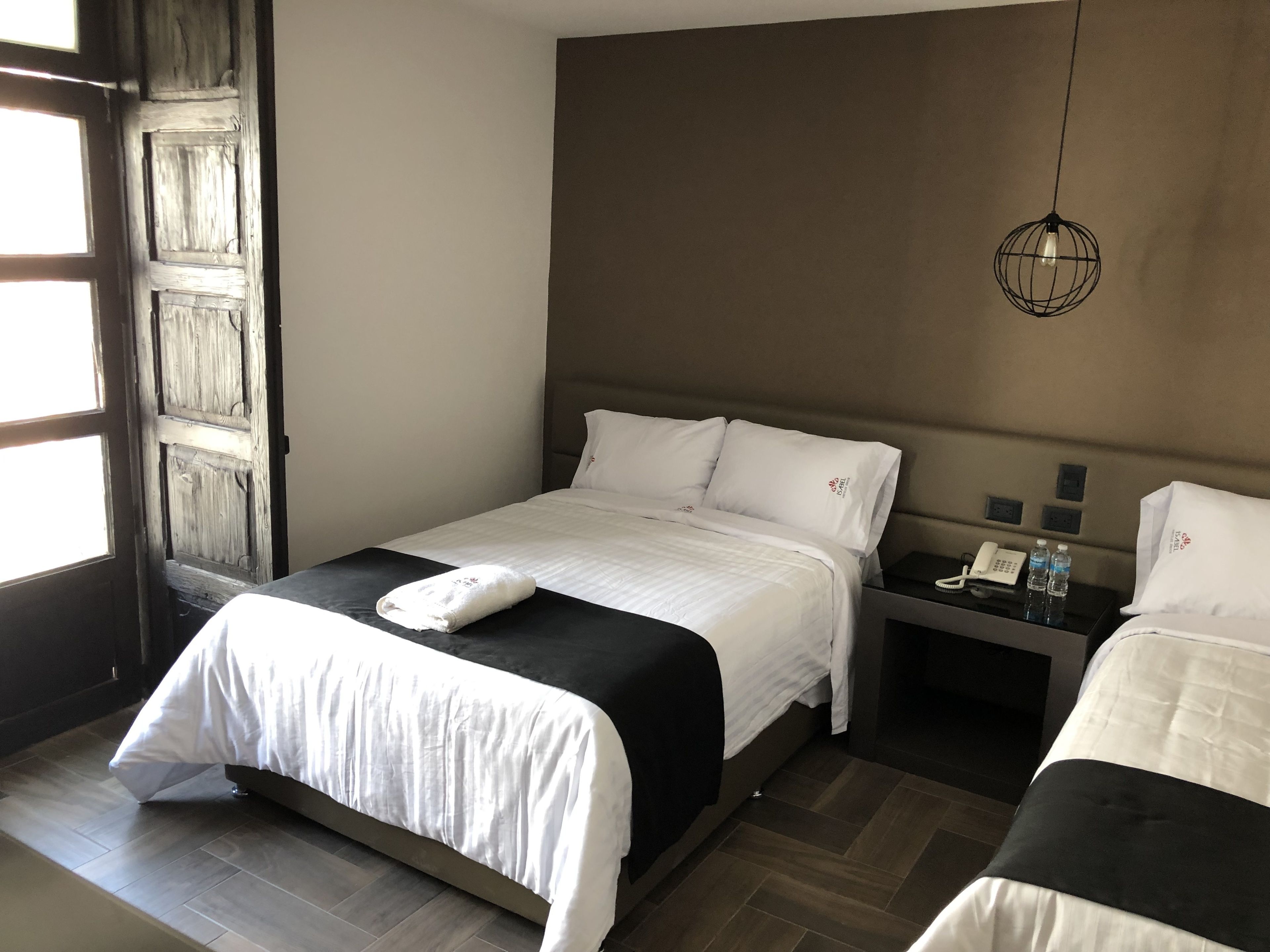 A hotel room with a bed, bedside tables, a telephone, and a hanging light fixture.