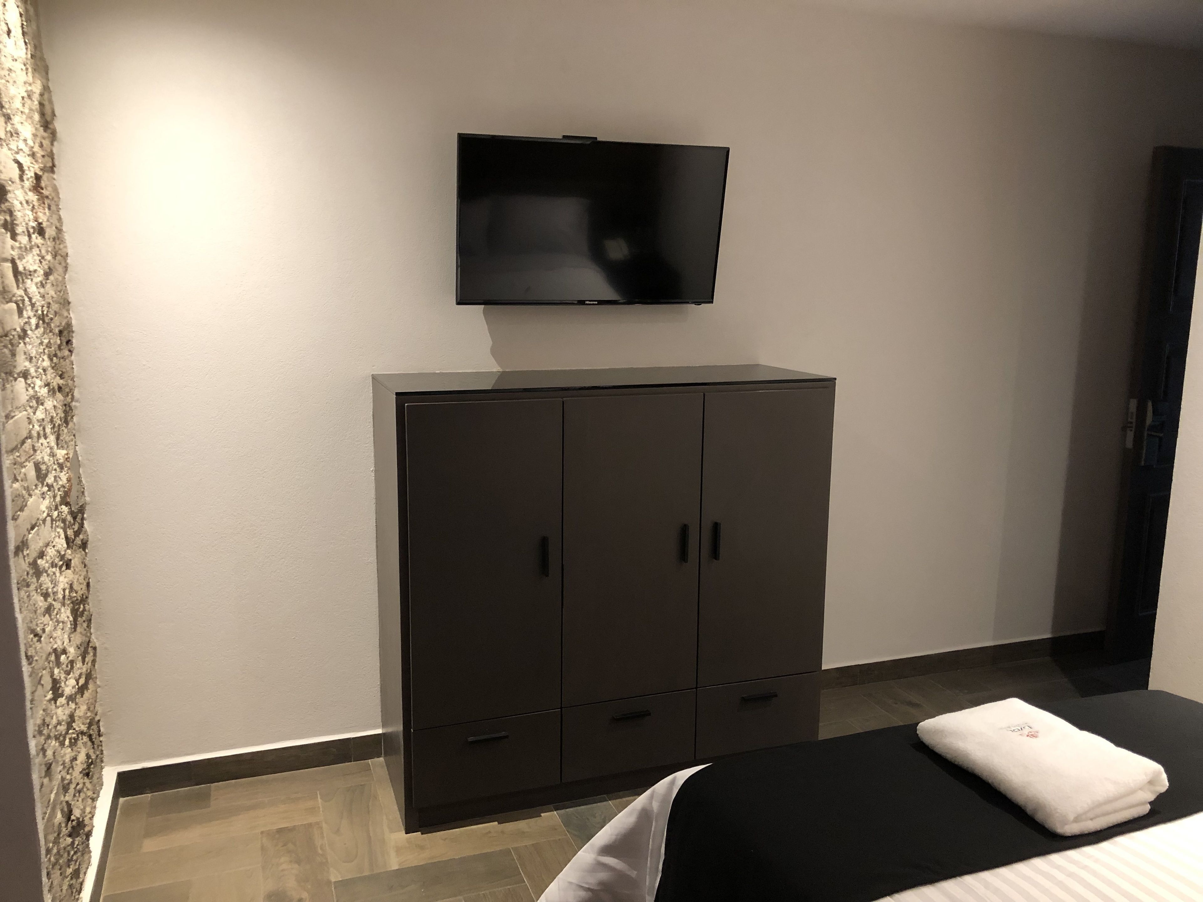 Un dormitorio con cama, un televisor de pantalla plana en la pared y un armario de color oscuro.