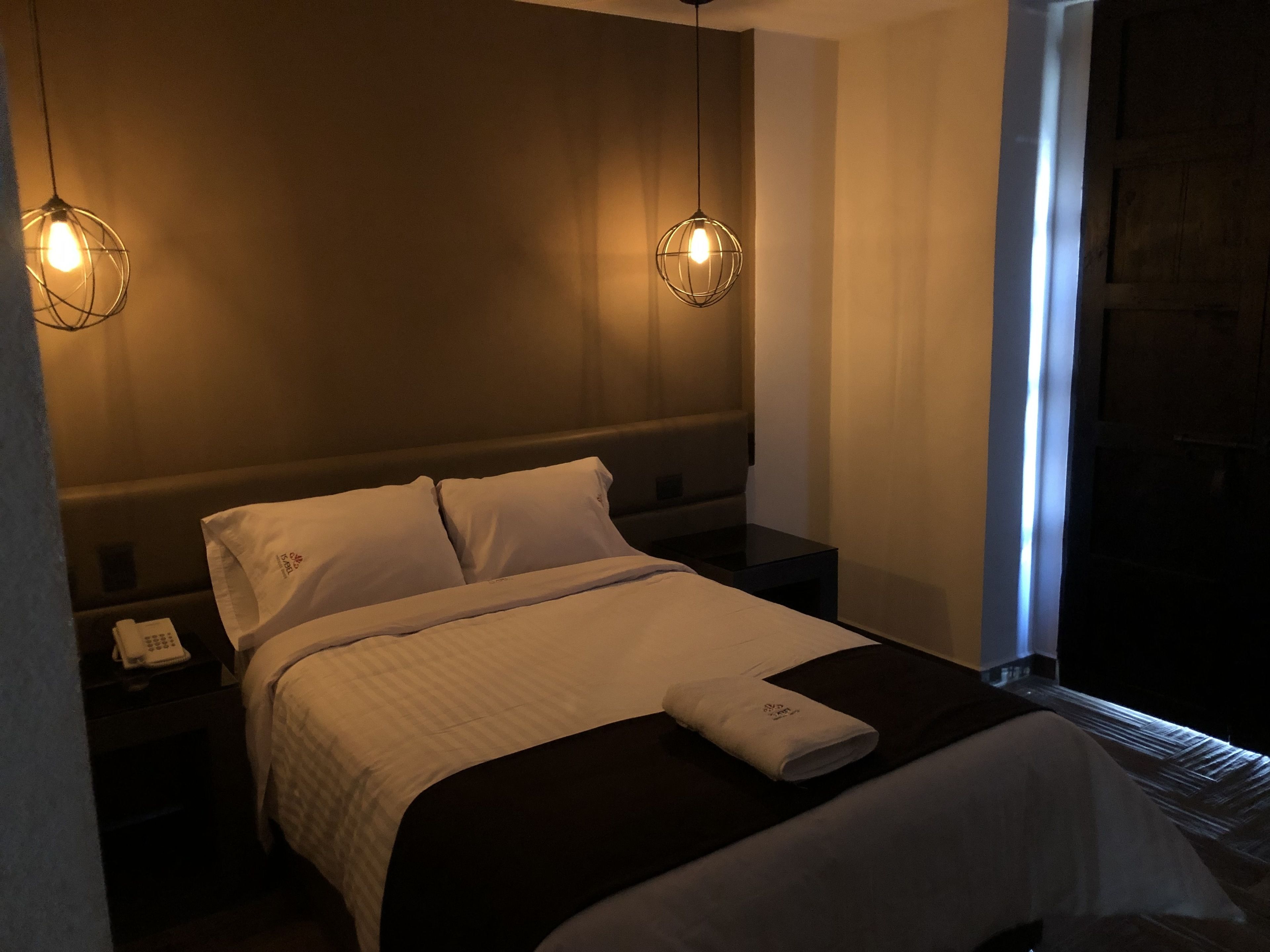 Une chambre d’hôtel comprenant un lit, deux tables de chevet, un téléphone et deux lampes suspendues.