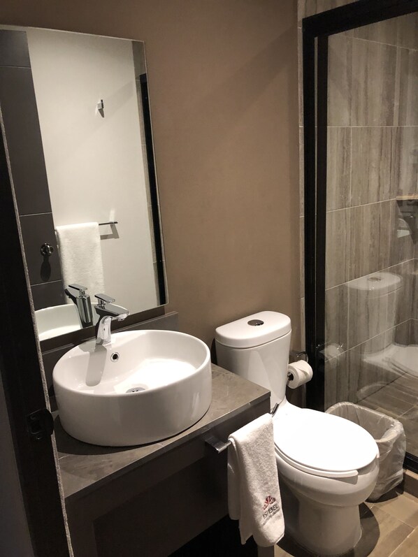A modern bathroom with a round sink, a toilet, and a glass shower enclosure.
