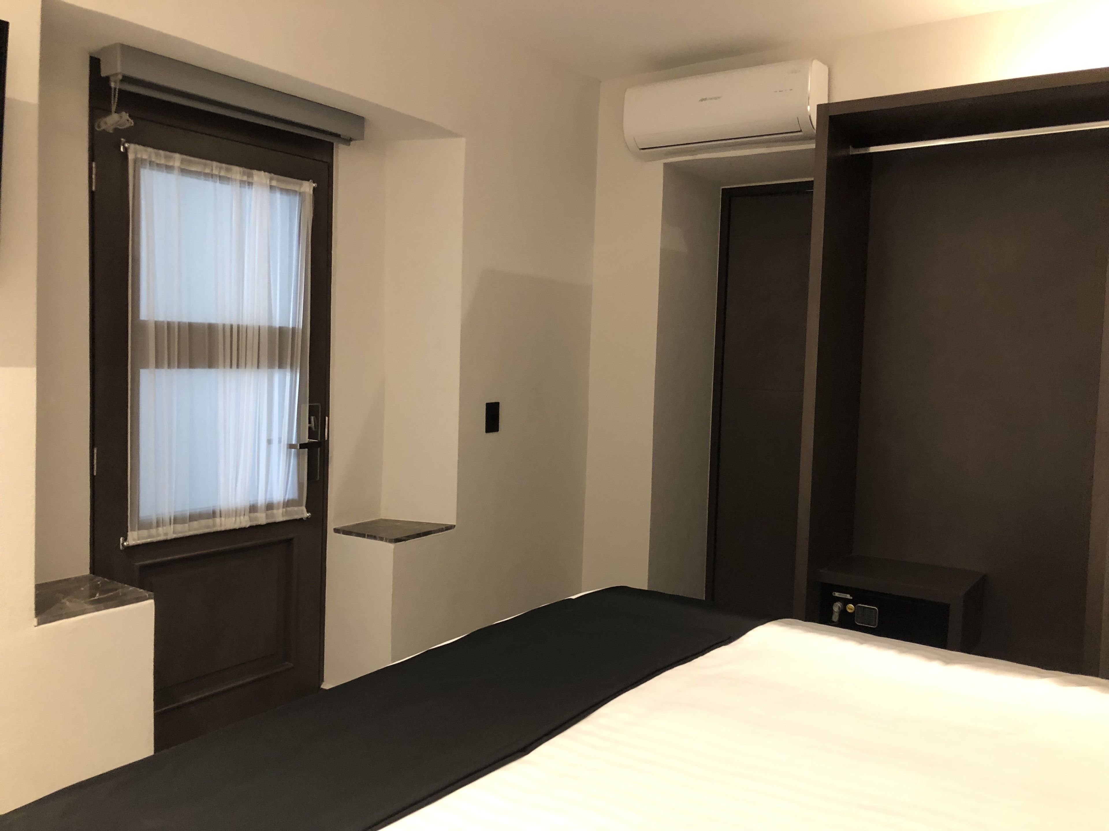 Een hotelkamer met een bed, een raam met gordijnen, een deur en een airconditioning.