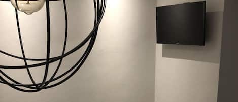Habitación de hotel con cama, lámpara colgante, televisor de pantalla plana en la pared y mesita de noche.