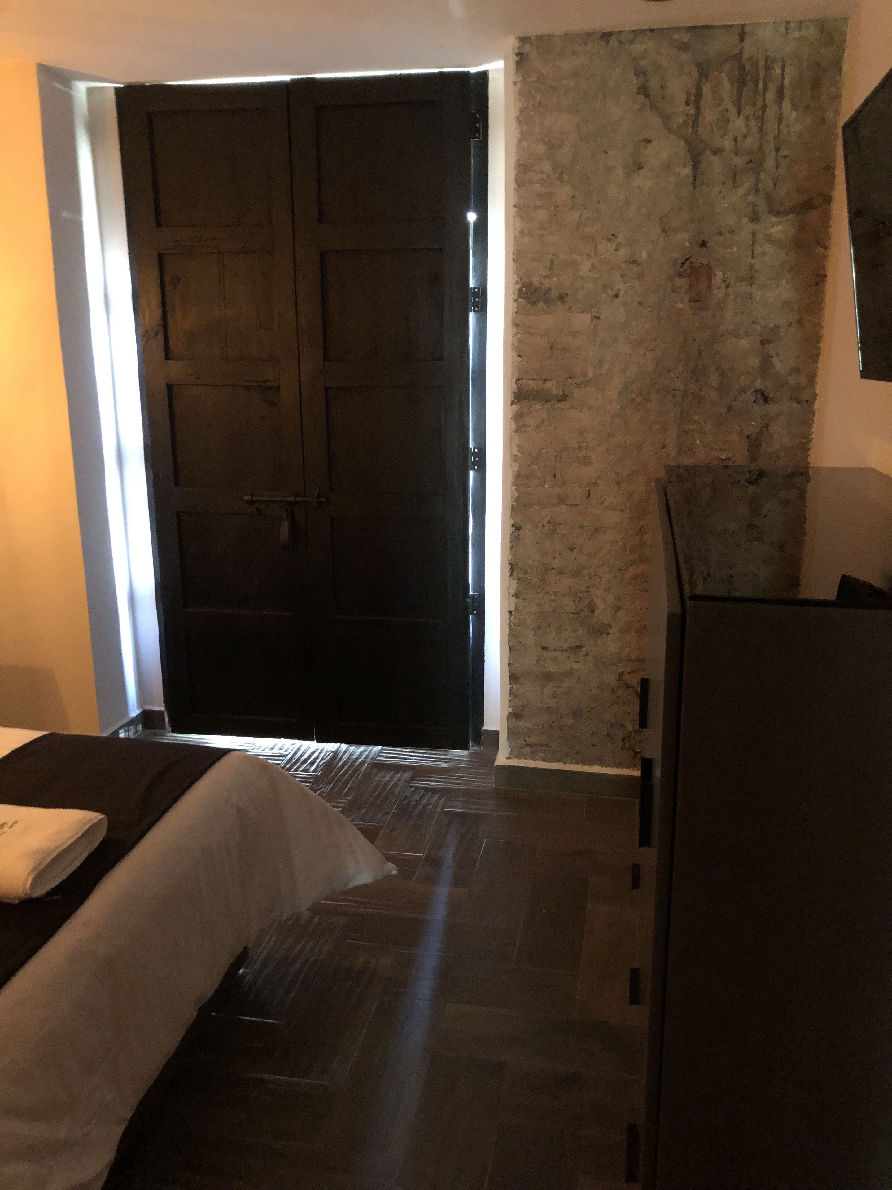 Una habitación de hotel con una puerta grande de madera, una pared de ladrillo y una cama con edredón blanco.