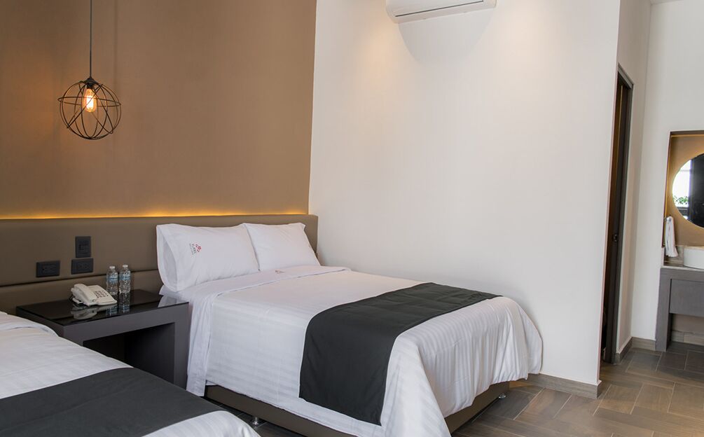 Ein Hotelzimmer mit zwei Betten, einem Nachttisch mit Telefon und Wasserflaschen, einer Wand-Klimaanlage und einer Pendelleuchte.
