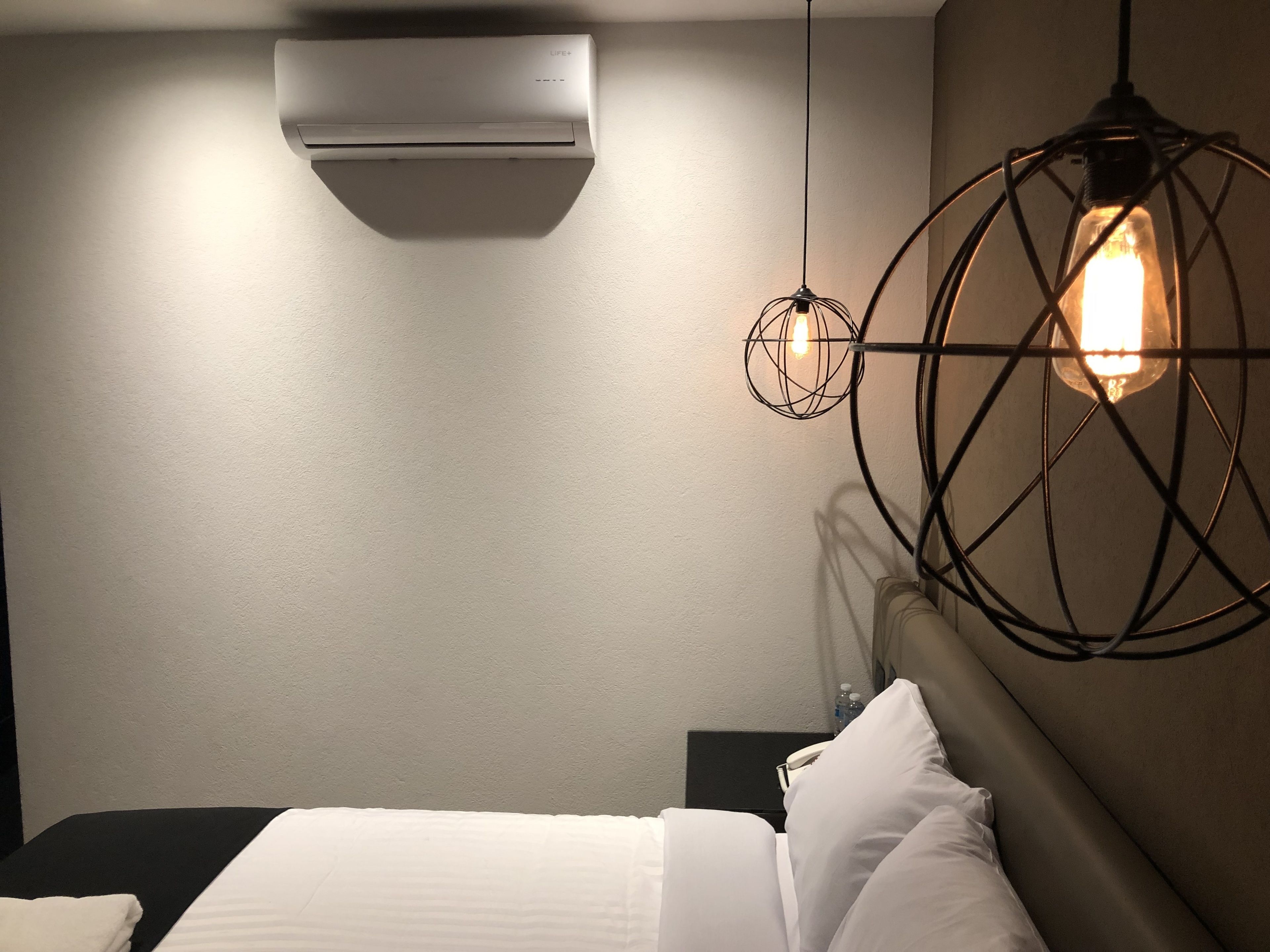 A hotel room with a bed, an air conditioner, and a unique pendant light fixture.