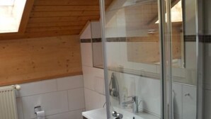 Une salle de bain avec un plafond en bois, des toilettes blanches, une cabine de douche en verre et un lavabo blanc avec un miroir au-dessus.