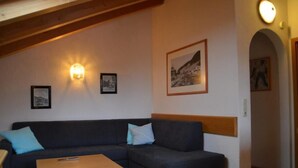 Un salon chaleureux avec un canapé aux couleurs sombres, une table basse en bois et un luminaire fixé au mur.