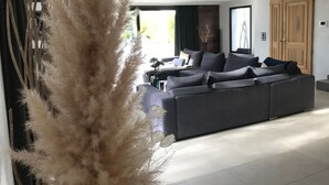 Una sala moderna con un amplio sofá modular gris, una planta decorativa alta y una puerta de madera.