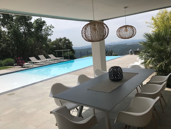 A poolside area with a table and chairs, a covered seating area, and a view of the pool and mountains.