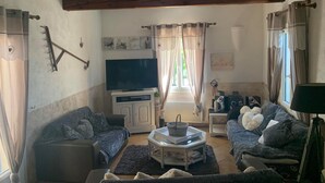 Uma sala de estar aconchegante com TV, dois sofás, uma mesa de centro e uma janela com cortinas.