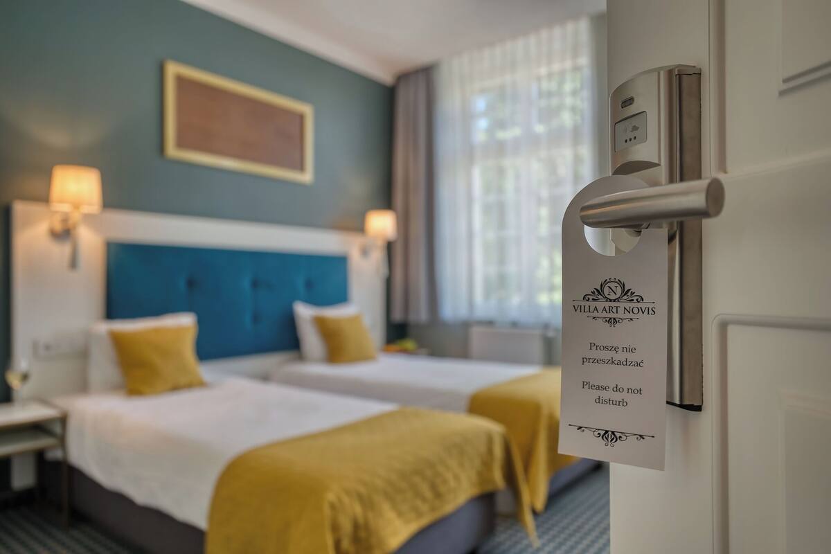 Una habitación de hotel con dos camas, un cabecero azul y un letrero en la puerta.