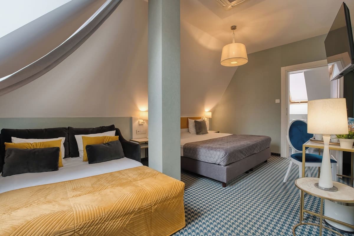 Habitación de hotel con una cama grande, una cama más pequeña, un escritorio, una silla, una lámpara y vistas al cielo.