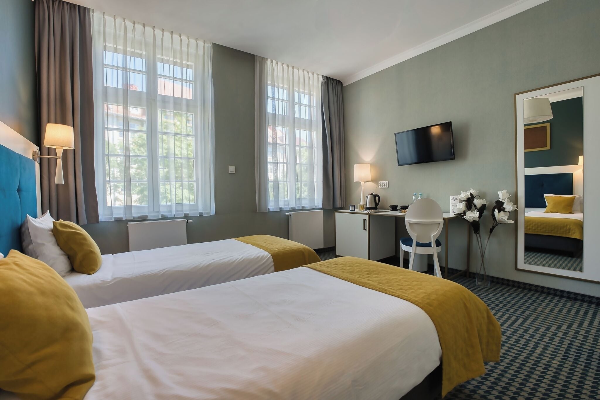 Habitación de hotel con dos camas, un escritorio, una silla, un televisor y un espejo grande.